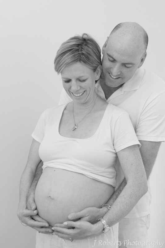 Couple smiling down at pregnant belly - B&W pregnancy portraits sydney